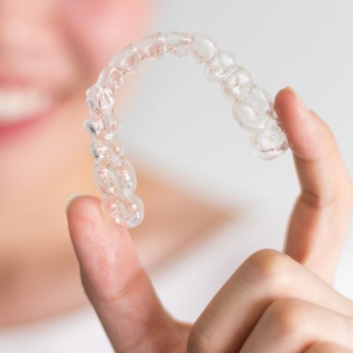 Smiling person holding a clear aligner