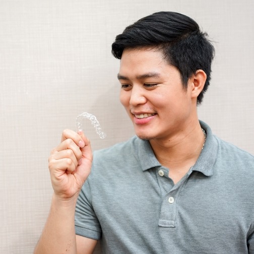 Man in gray polo shirt holding a clear aligner