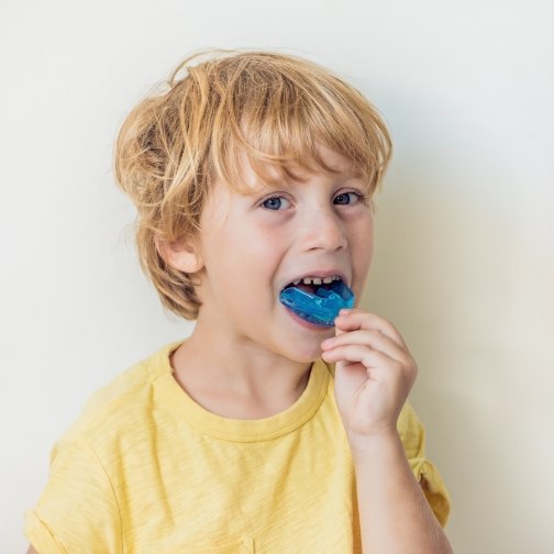 Young boy placing a blue athletic mouthguard over his teeth