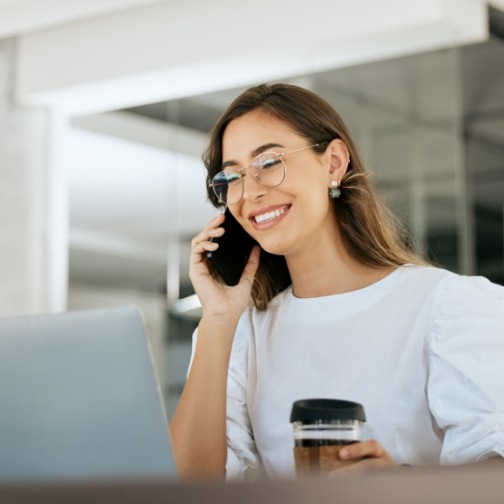 Woman talking on the phone while sitting at desk with coffee cup