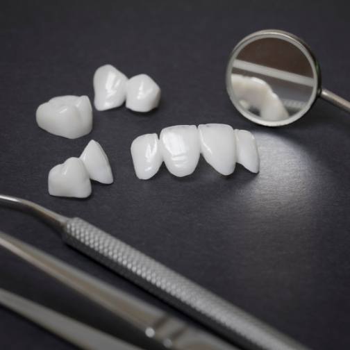 Several white dental crowns and veneers on table next to dental mirrors