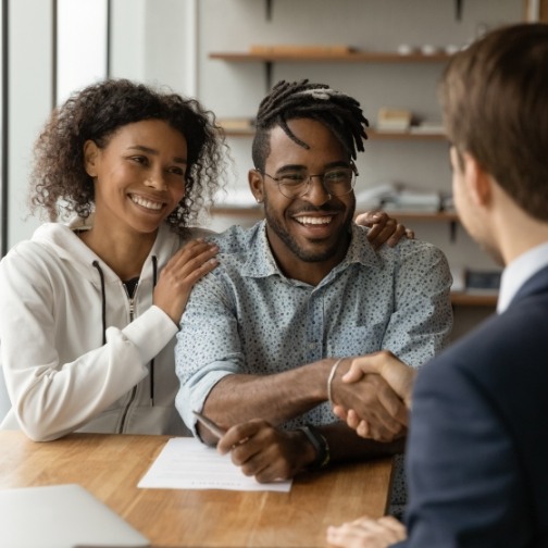 Smiling man shaking hands with person across desk