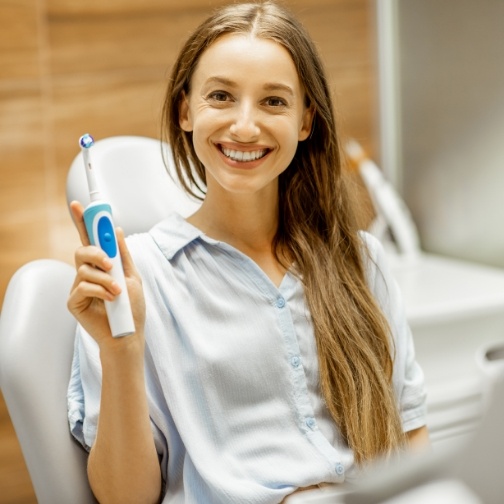 Smiling woman in dental chair holding electric toothbrush