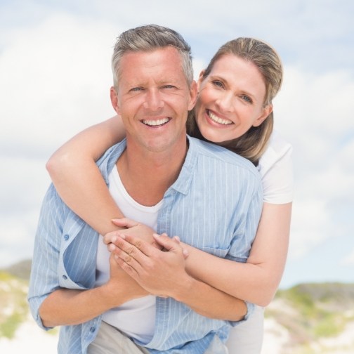 Senior couple hugging and smiling outdoors with dentures in Fort Worth