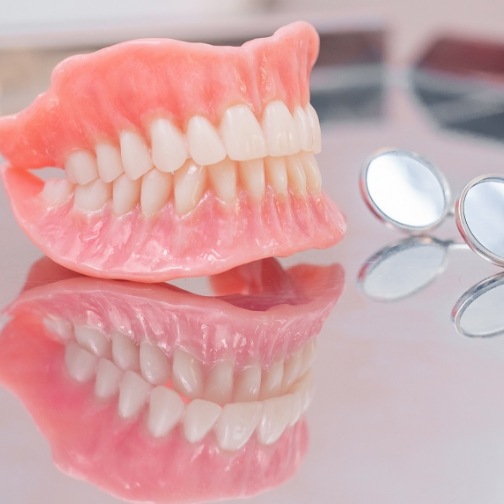 Set of full dentures resting on table next to dental mirrors
