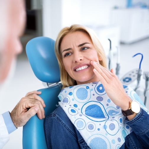 Woman wincing and holding her cheek while talking to emergency dentist in Fort Worth