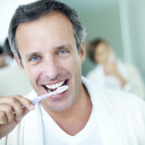 Man smiling while brushing his teeth