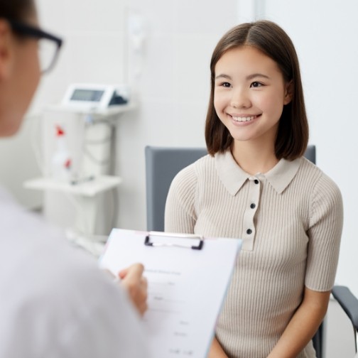 Woman smiling while her dentist writes on clipboard