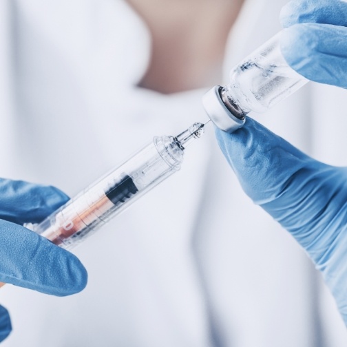 Dentist drawing syringe from vial with white liquid