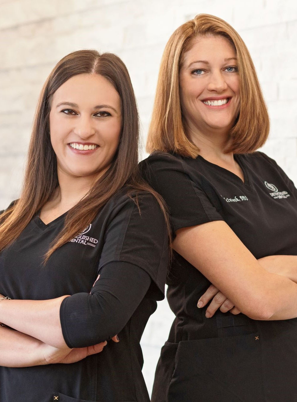 Two Fort Worth dentists smiling and standing back to back with arms crossed