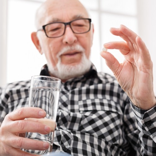 Senior man holding a pill and a glass of water