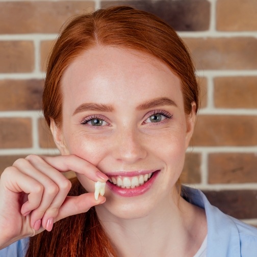 Smiling young woman holding an extracted tooth