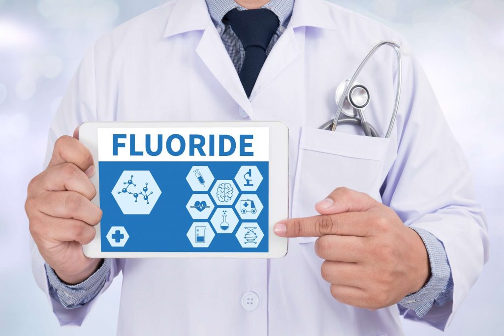 A dentist holding a sign that reads, “Fluoride”